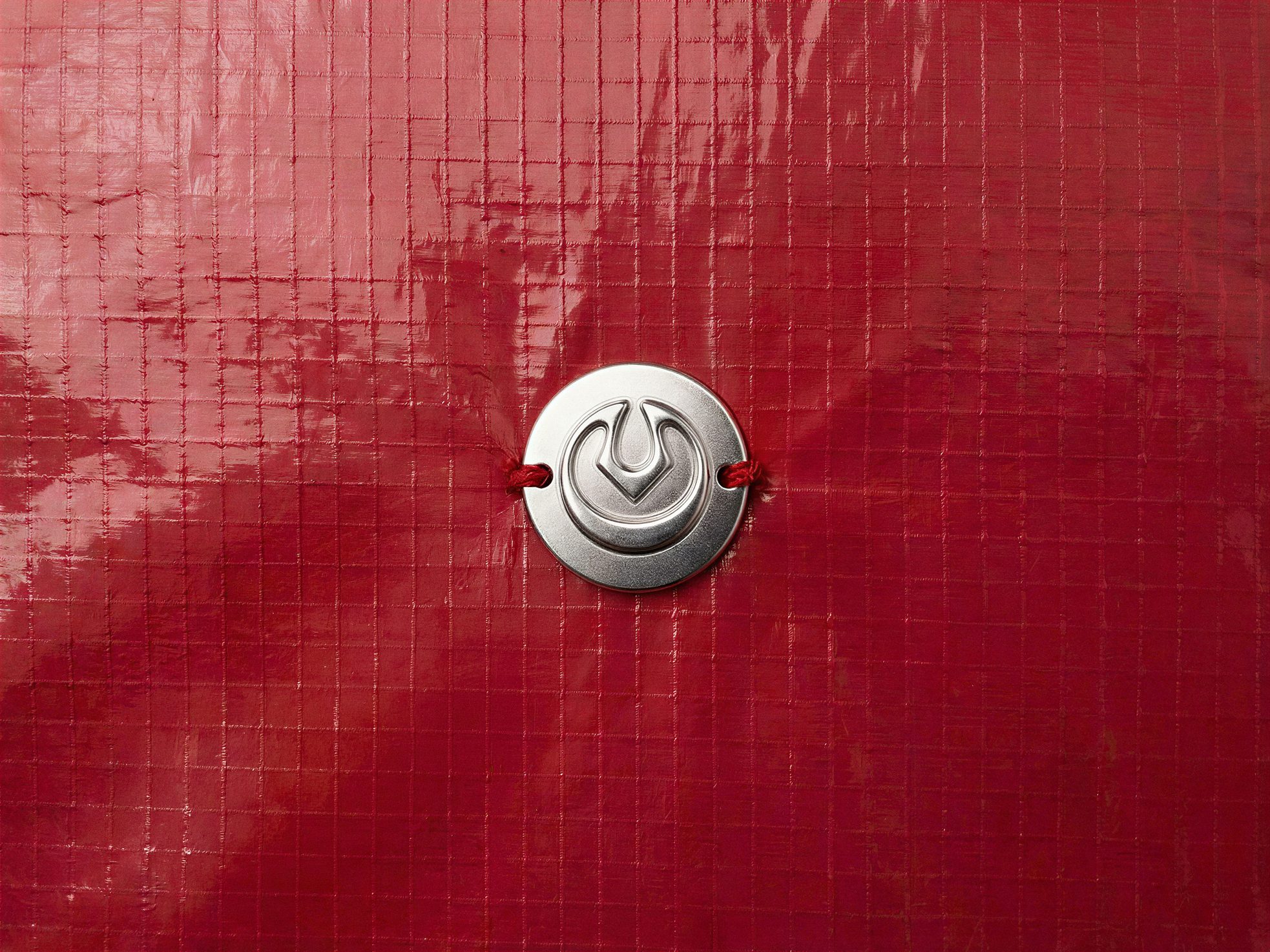 Varchu identity: round embossed metal logo badge on red ripstop